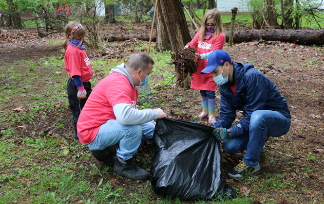 two young girls and their fathers putting leaves in a garbage bag